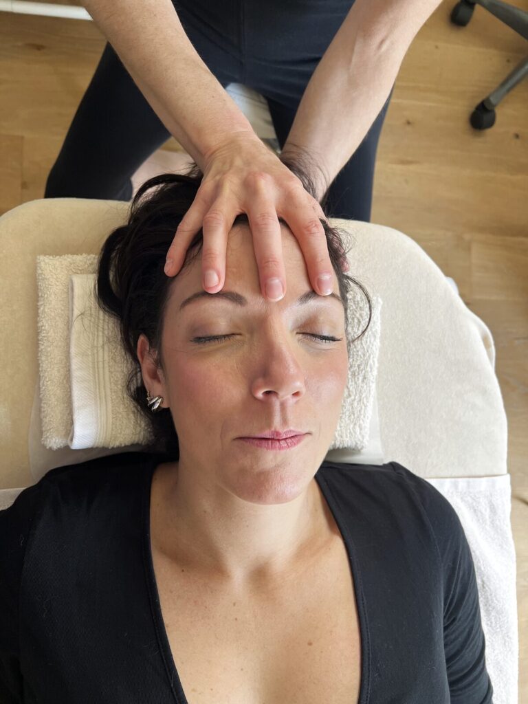 Séance de fasciathérapie : mains posées sur le front, patiente allongée
